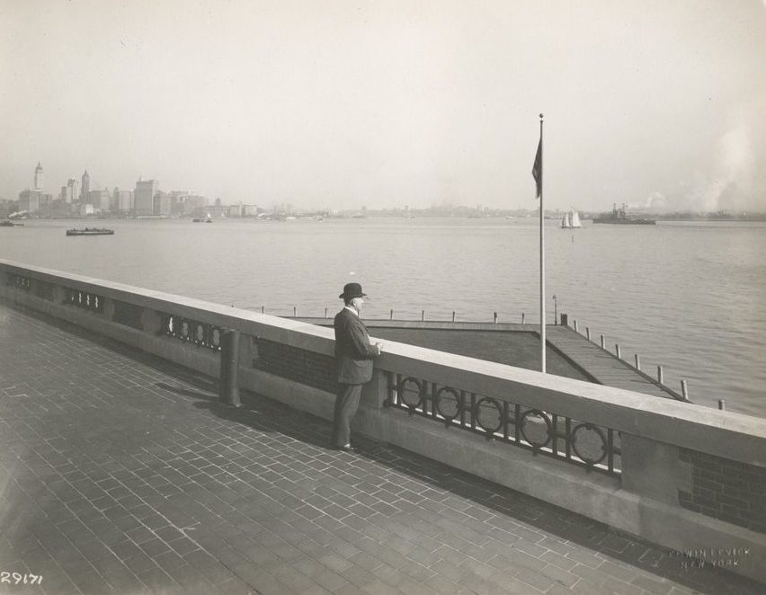 "A derby-topped gentleman observing the harbor from the observation roof on one wing of the Immigration Station. The gentleman is possibly William Williams, Commissioner of Immigration at Ellis Island form 1902-5 and 1909-13, from whose estate these photographs came. The New York skyline, showing the nearly-completed Woolworth Building tower, is at the left."