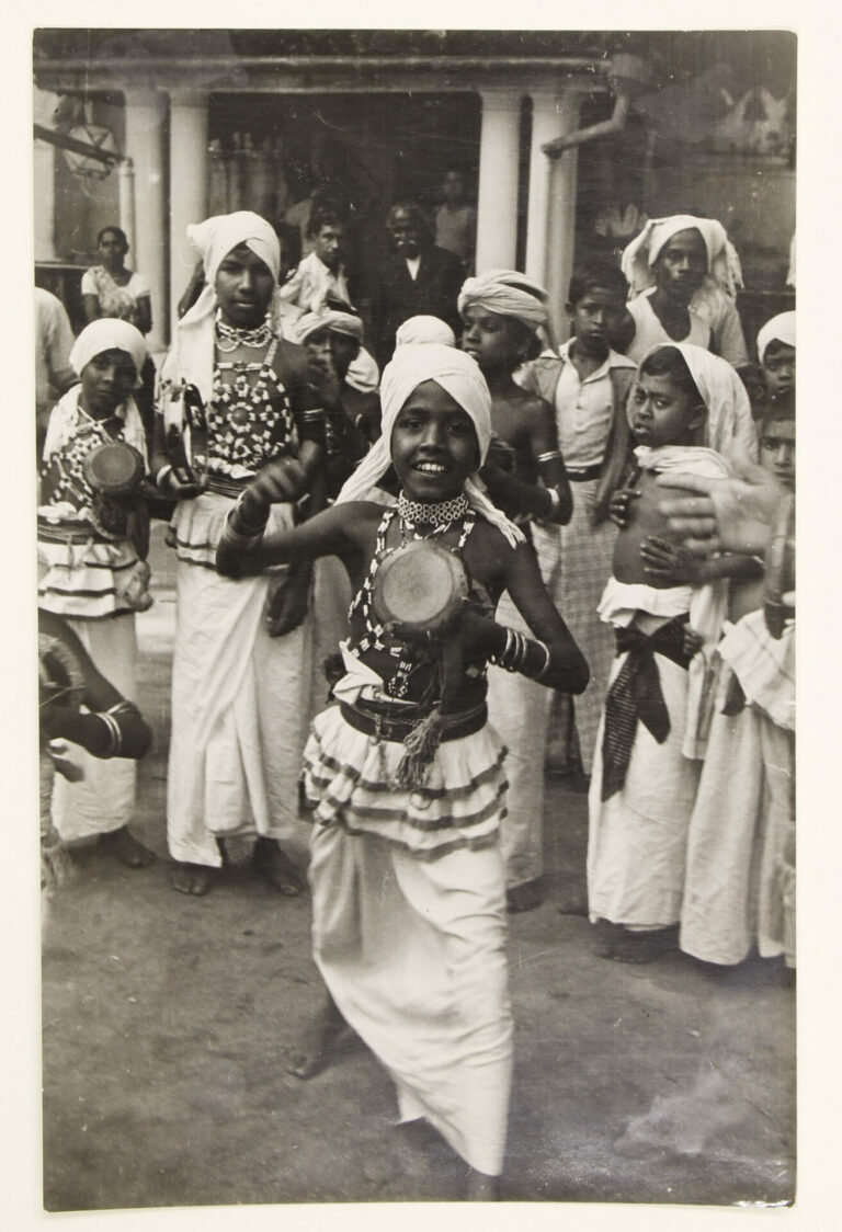 Dynamic image of boy with a drum-like instrument in the foreground, with others people a few steps behind him.