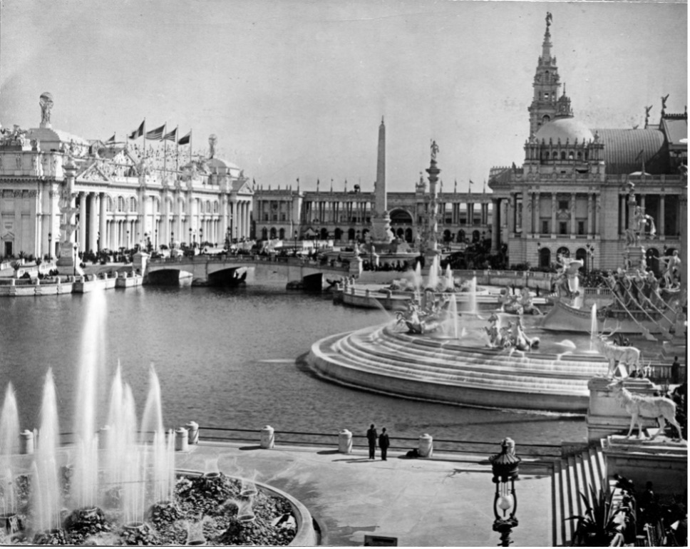 Grand fountains around a bay surrounded by buildings in the classical style. Black and white historical photo of the Columbian Fountains at the World's Columbian Exposition.