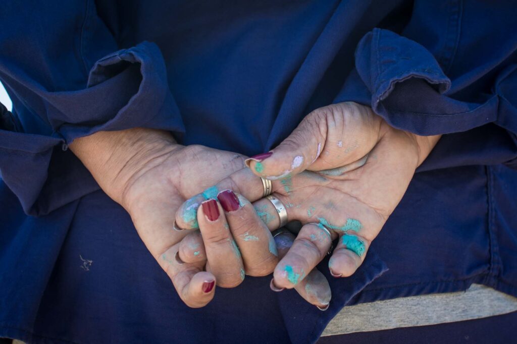 Female hands lightly clasped behind the back with rings, red nail polish and blue paint splotches.