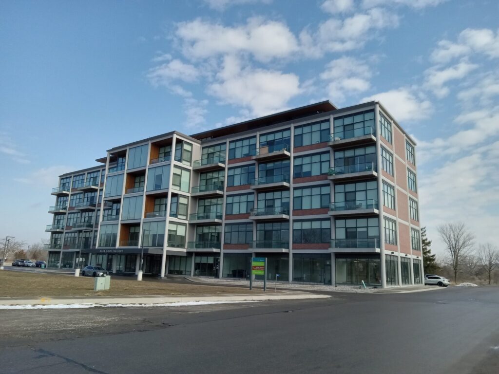 Rectangular building with an extra twelve units protruding from the middle. Balconies and commercial storefronts can be discerned.